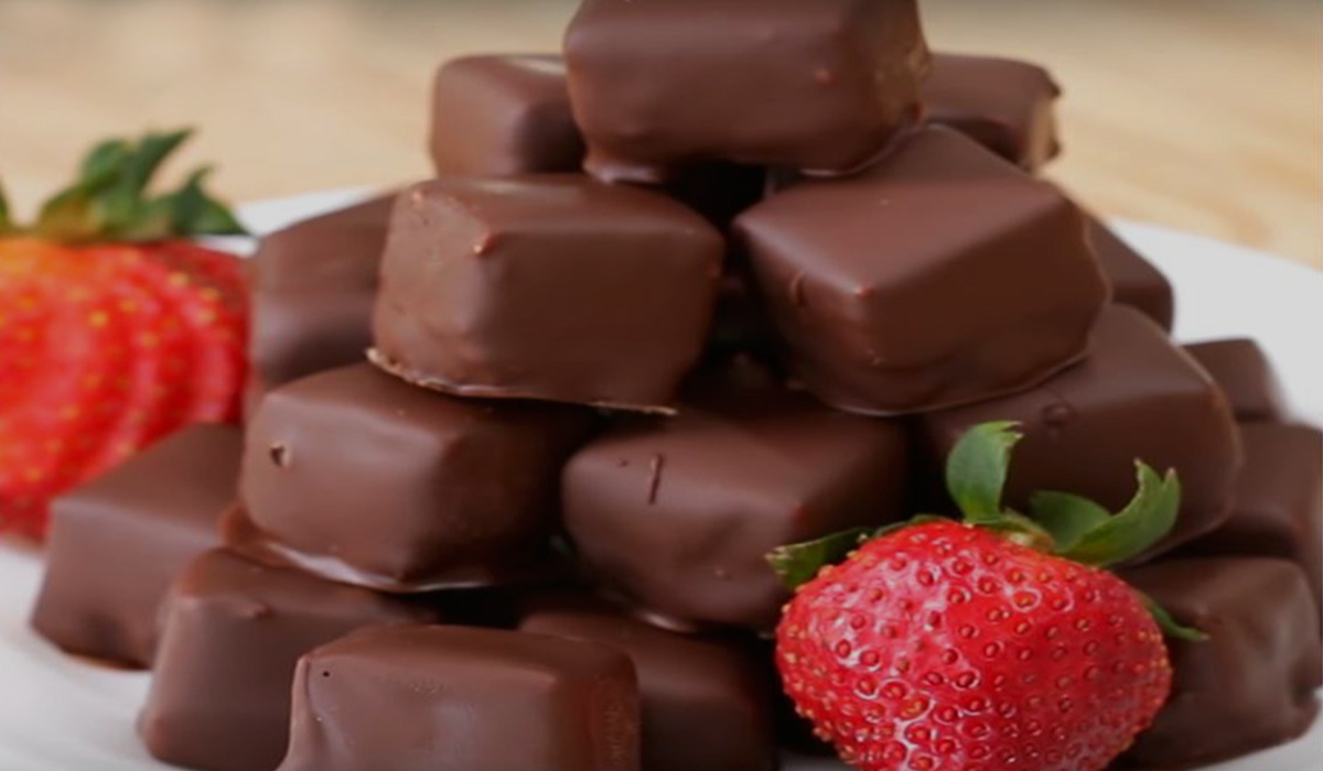 Close-up of a cheesecake bite with a rich chocolate shell and creamy filling inside.