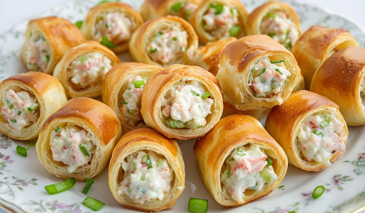 A batch of freshly baked crab and cream cheese crescent rolls, garnished with fresh herbs and served on a wooden cutting board.