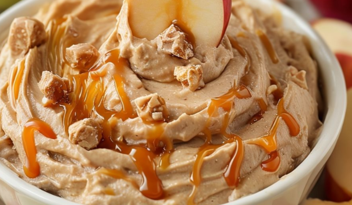 A bowl of creamy caramel apple dip topped with a drizzle of caramel sauce and served with sliced apples.