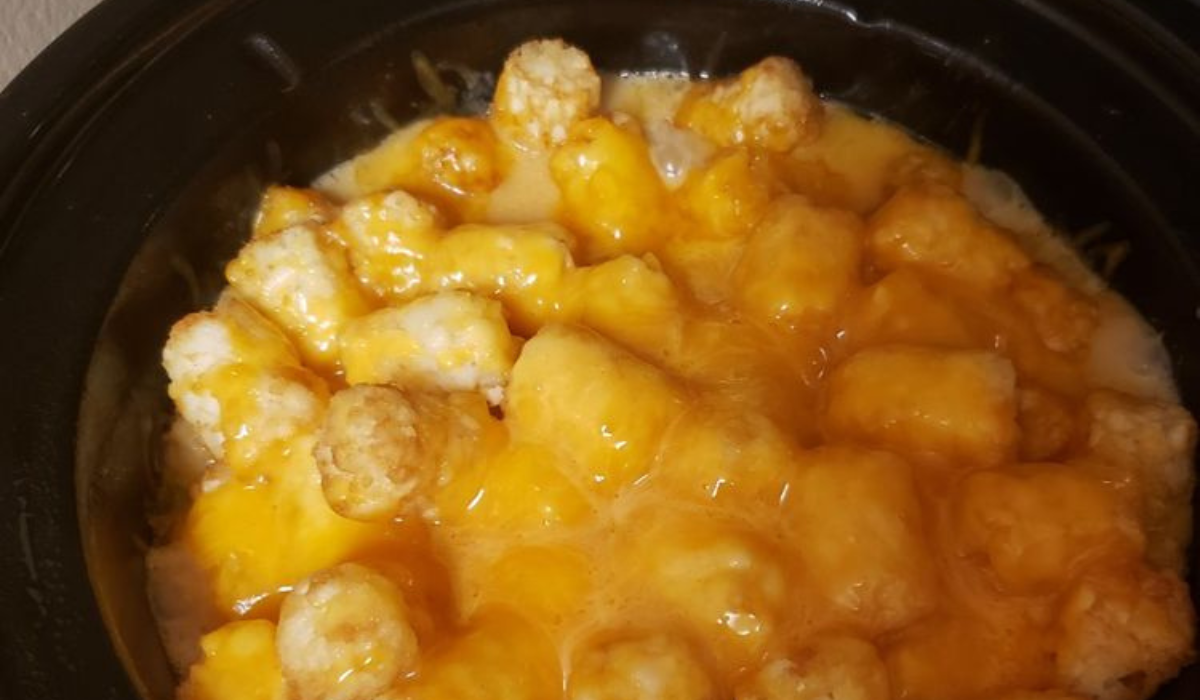 A slow cooker filled with bacon cheeseburger tater tot casserole, golden and bubbling with melted cheese on top.