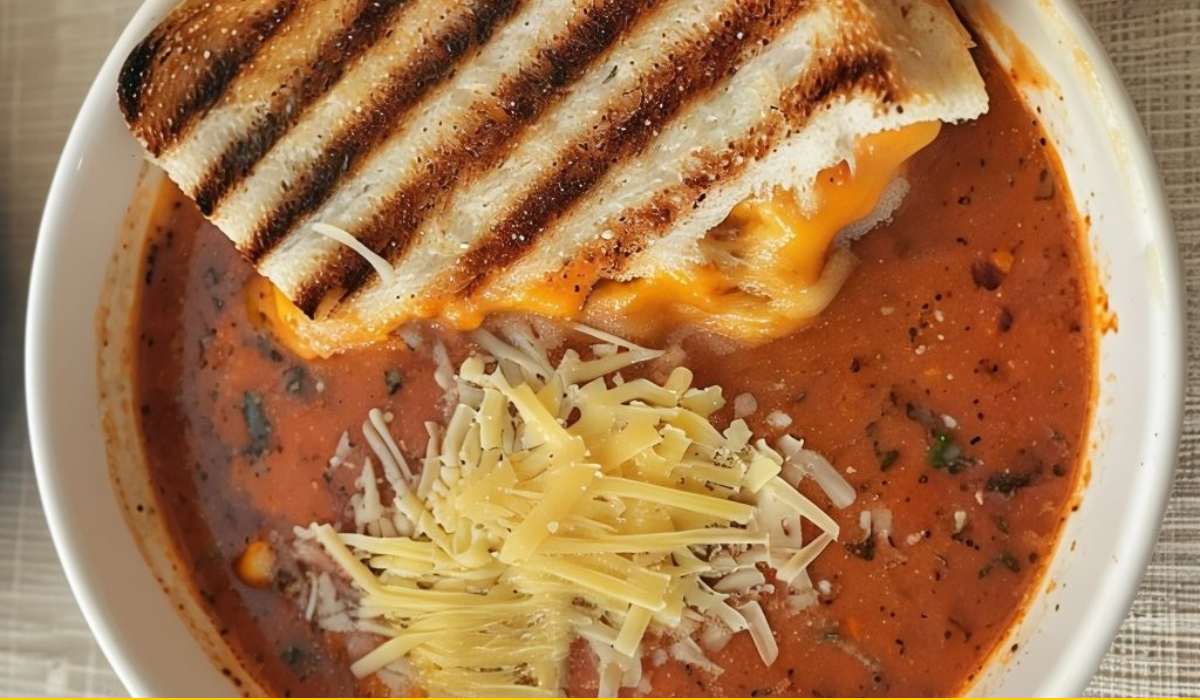 Bowl of creamy tomato soup topped with herbs and served with a grilled cheese sandwich.