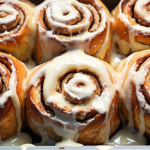 Freshly baked banana bread cinnamon rolls in a pan with cream cheese icing melting over the top